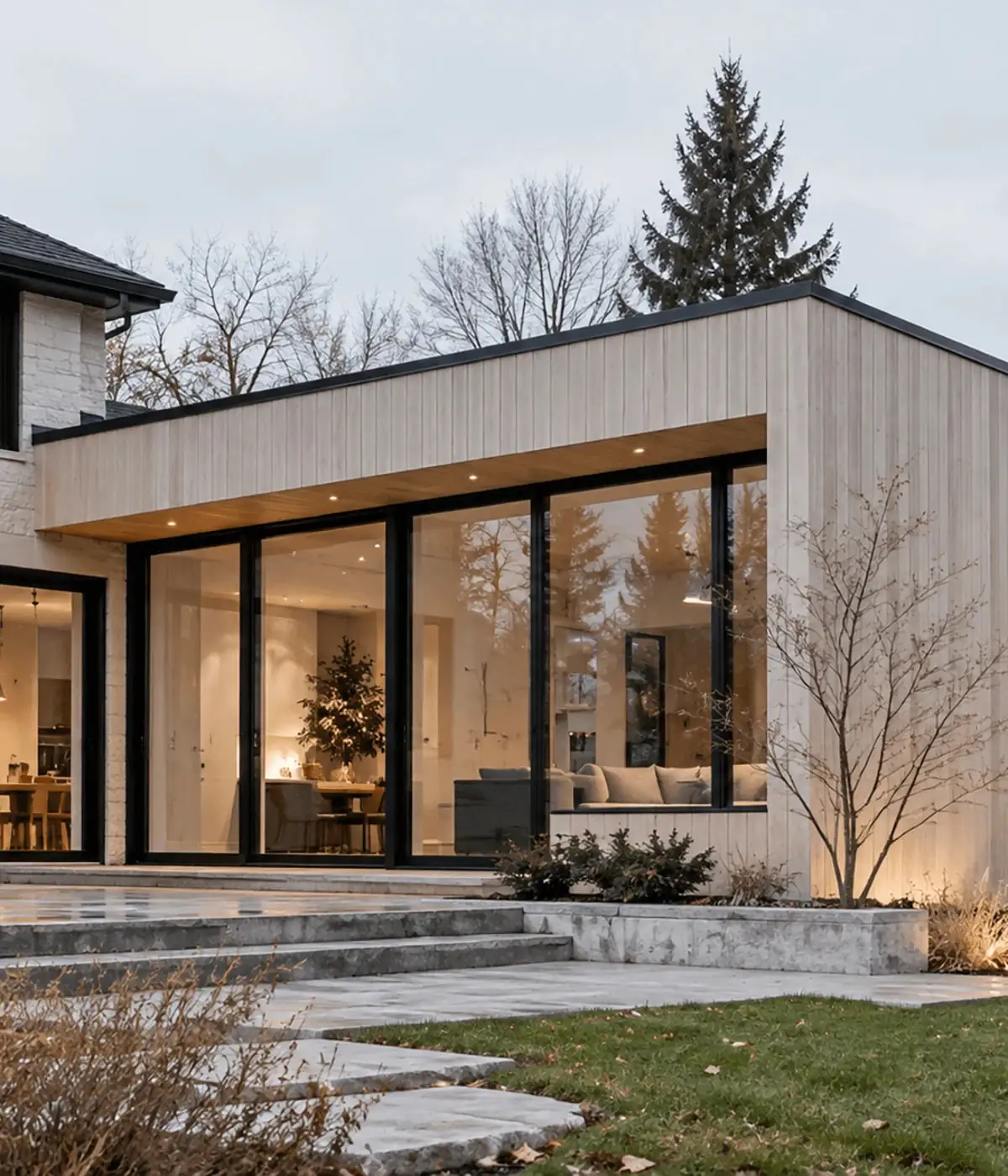 House extension with pale vertical wood cladding and floor-to-ceiling glass doors at dusk